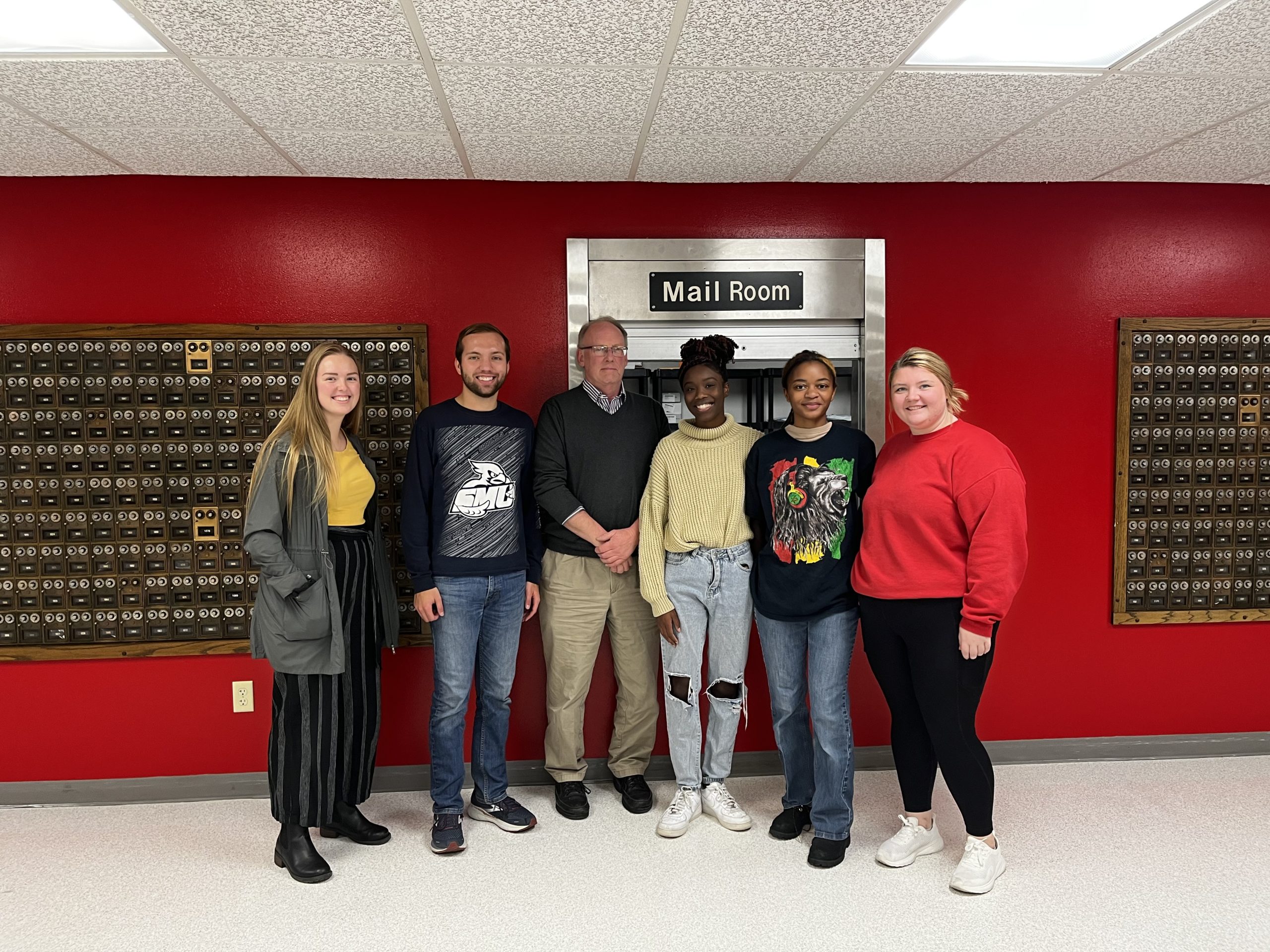 Five student workers and the mailroom coordinator standing in front of student mailboxes.