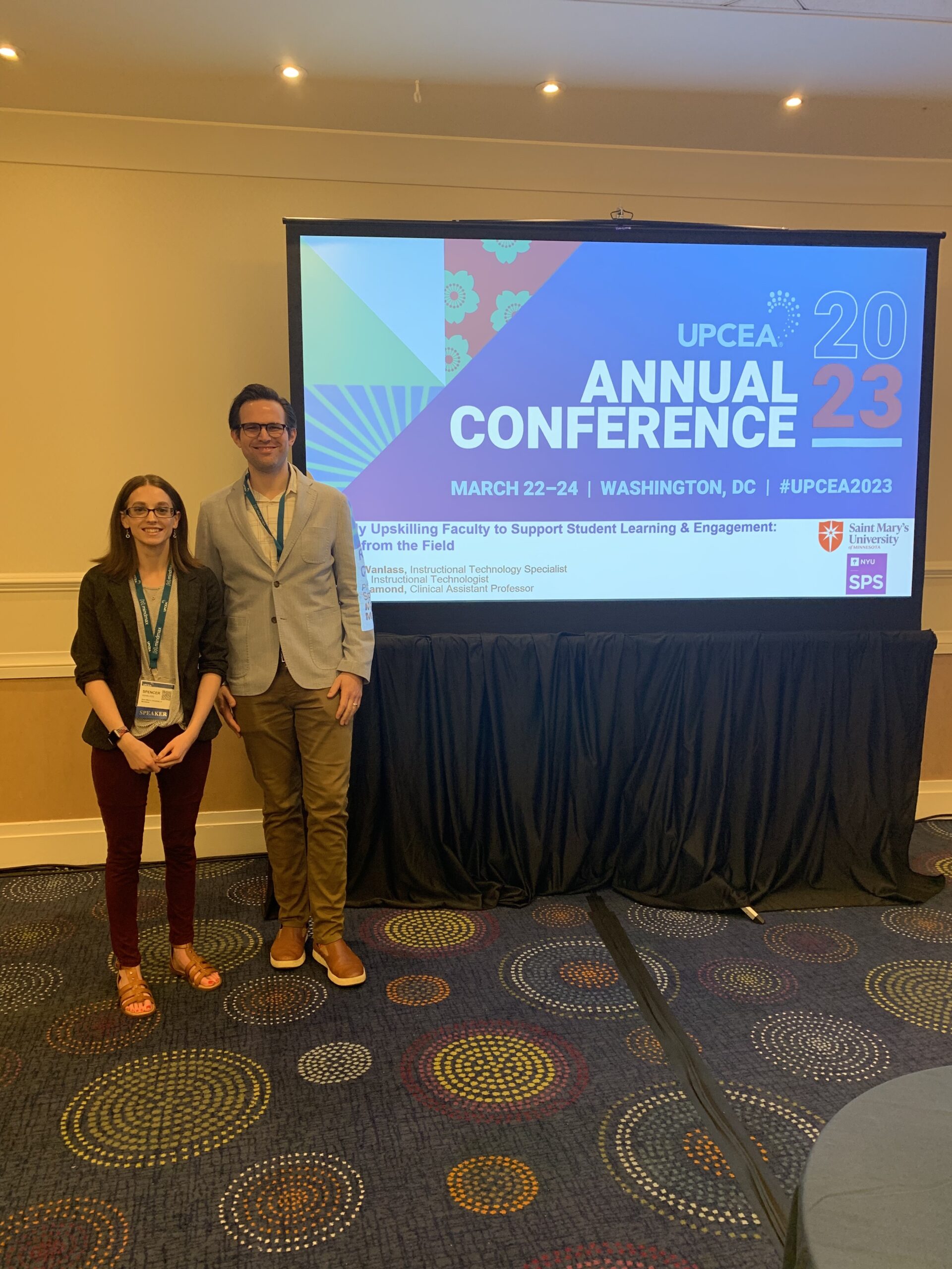 The picture shows Spencer Wanlass and Matt Isaia in their presentation room in front of the screen with their slide title.