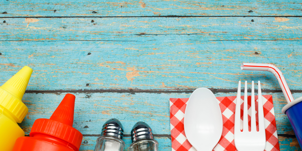 A picture of a yellow mustard bottle, red ketchup bottle, and matching salt and pepper shakers resting on a blue picnic table.