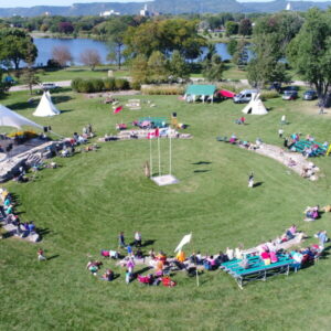 Drone captured photograph of Unity Park. Spectators are seated around the powwow dancing arena. Lake Winona is apparent in the background