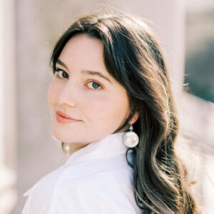 Woman with long brown hair, head turned over shoulder and slightly smiling while looking straight ahead.