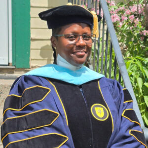 Lydia Majors-Roland, smiling, wearing cap and gown for graduation.