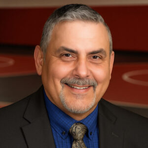 Smiling man with facial hair wearing a suit jacket, dress shirt, and tie.