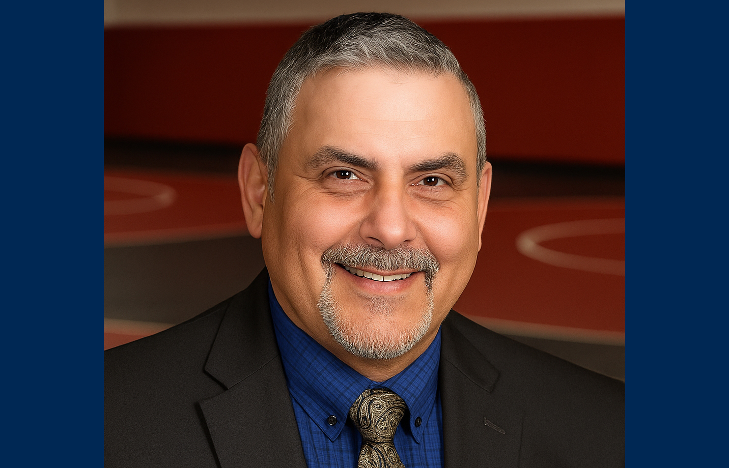Smiling man with facial hair wearing a suit jacket, dress shirt, and tie.